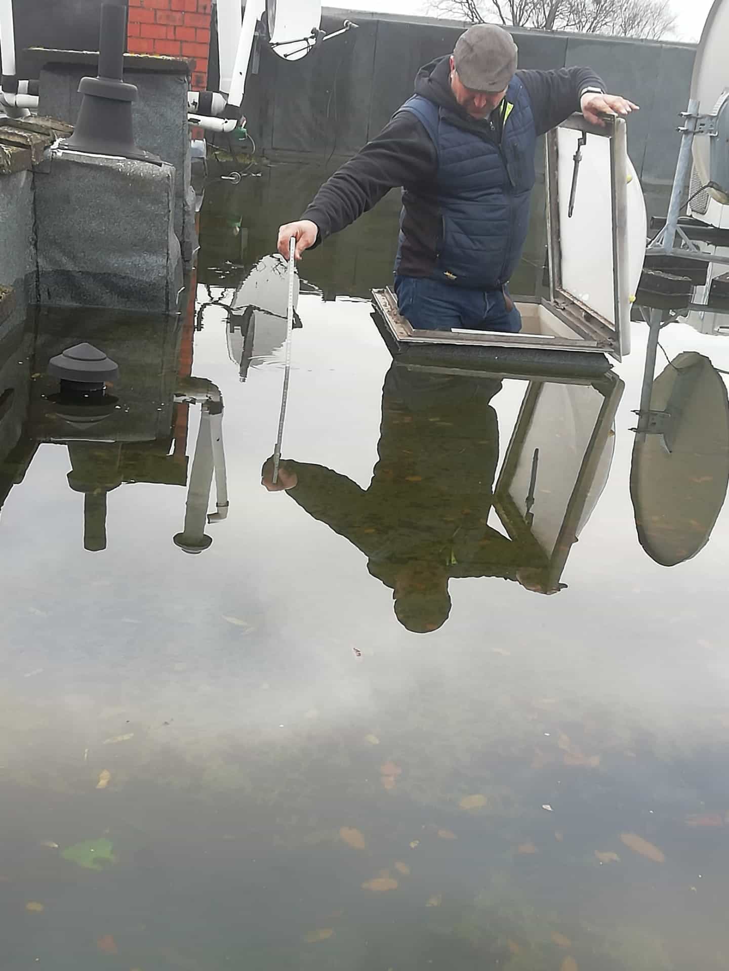 Dakwerker controleert waterstand en afvoer op plat dak tijdens onderhoud